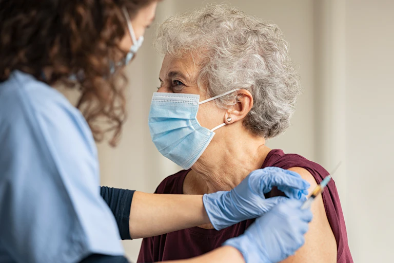 An elderly woman in a mask being vaccinated