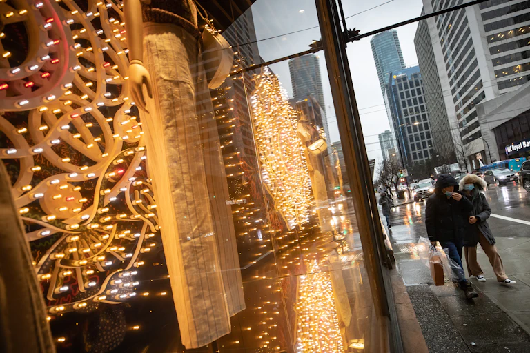 People wearing face masks walk past a store window alit with Christmas lights.
