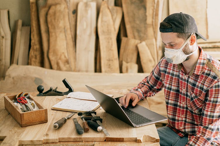 A man wearing a mask sits in front of his laptop.