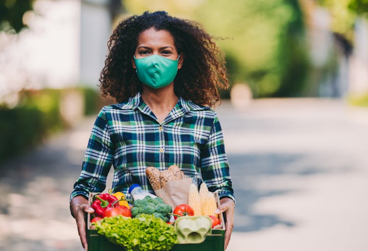 Woman in a mask holding a basket of vegetables and freshly baked bread