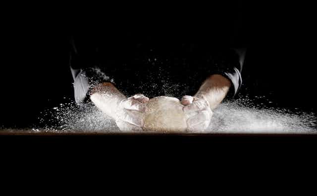 Two hands knead dough against a black background