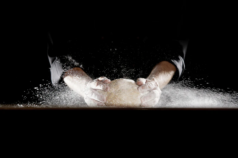 Two hands knead dough against a black background