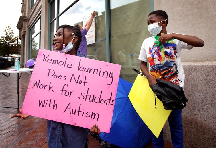 Girl holds handmade poster that reads: 'Remote learning does not work for students with autism'