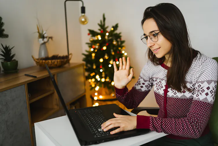 A woman sits on her laptop and waves at it