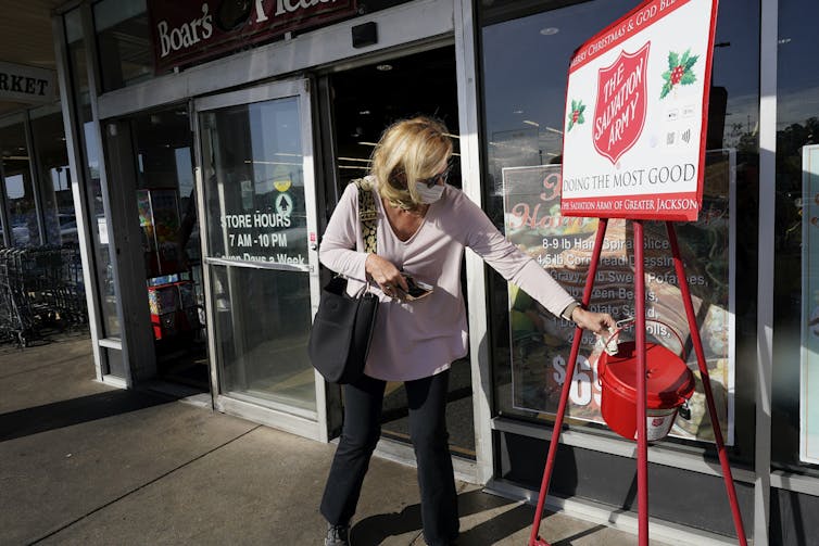 Woman places money into a Salvation Army Christmas appeal bucket.