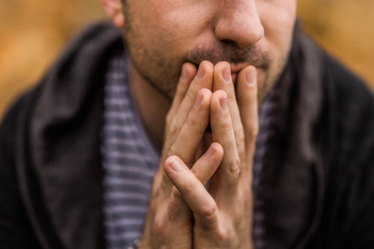 anxious young man clasps hands with chewed nails in front of face