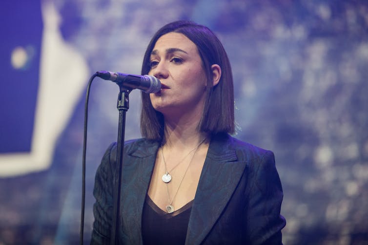 Musician Nadine Shah singing into microphone.