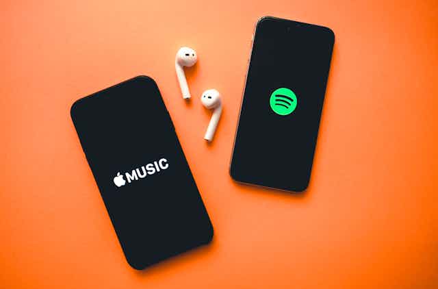 Two phones on orange background with earphones showing apple music logo and spotify logo.