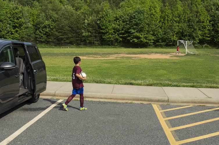 Boy holding ball walks away from car