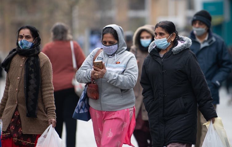 Three women wearing masks walk down the street with shopping bags.