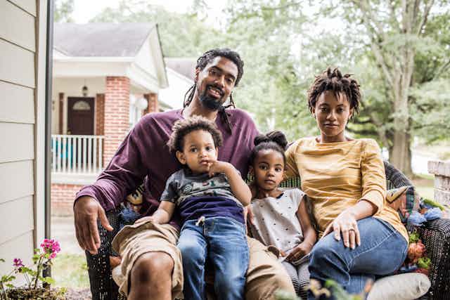 A Black family with father, mother and two children, sitting on their porch.
