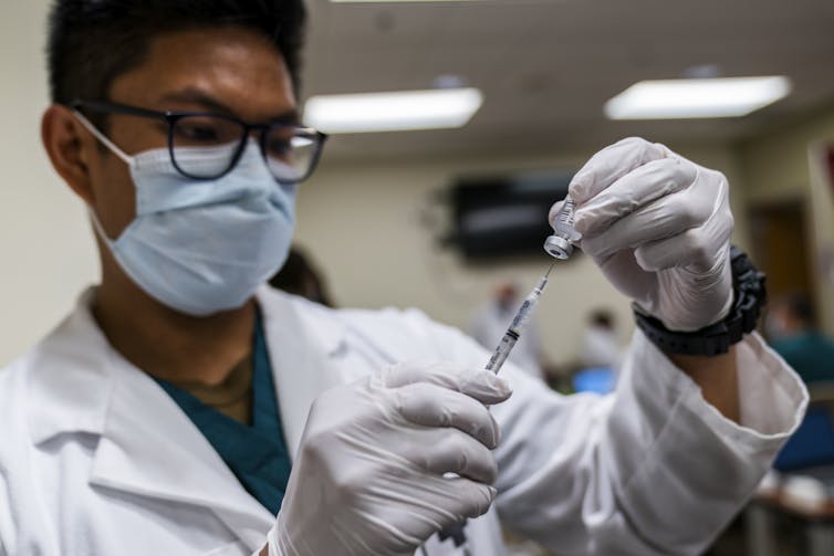 A man wearing a mask and gloves handles a COVID-19 vaccine.