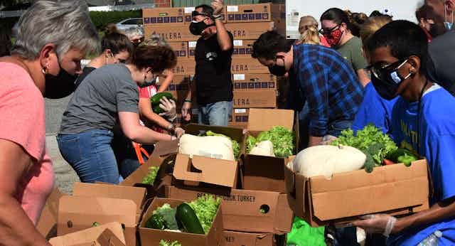 People in masks surrounding boxes of produce