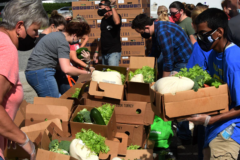 People in masks surrounding boxes of produce