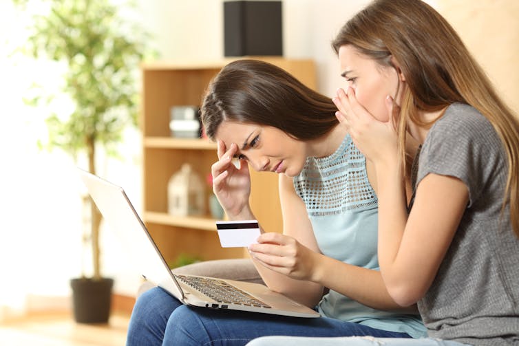 Two girls look shocked and disappointed while they stare at a computer screen.