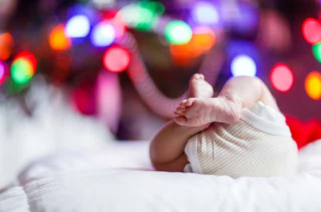 Newborn baby on back in front of Christmas tree lights