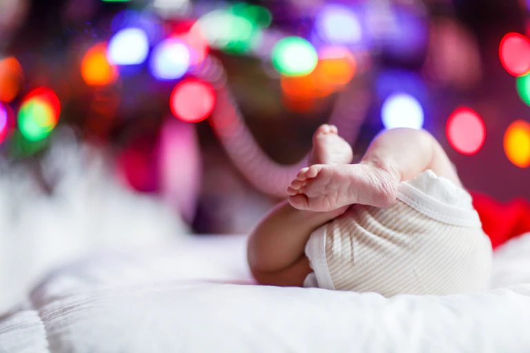 Newborn baby on back in front of Christmas tree lights