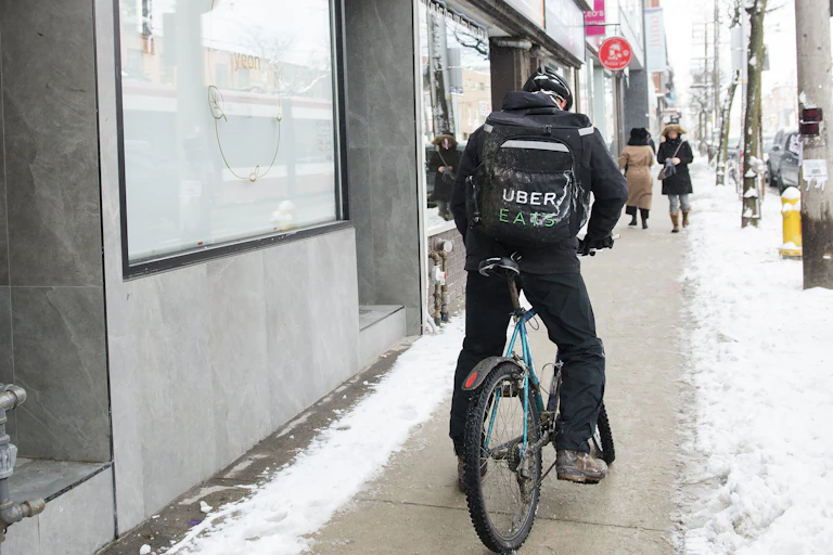 An Uber Eats courier on a bike pick ups an order for delivery on a snowy city street.