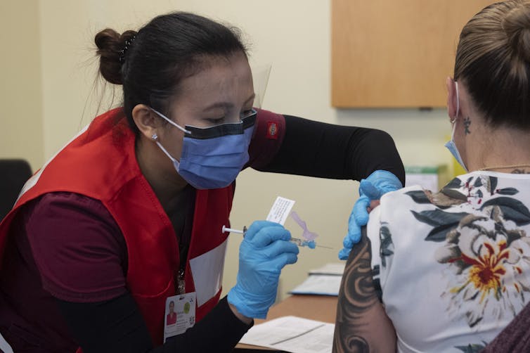 A nurse wearing a mask vaccinates another woman.