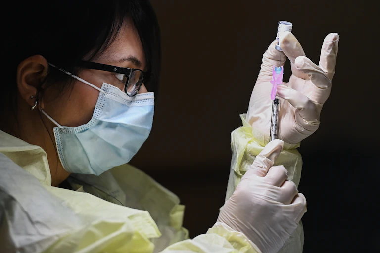 A woman in a mask fills a vaccine into a syringe.