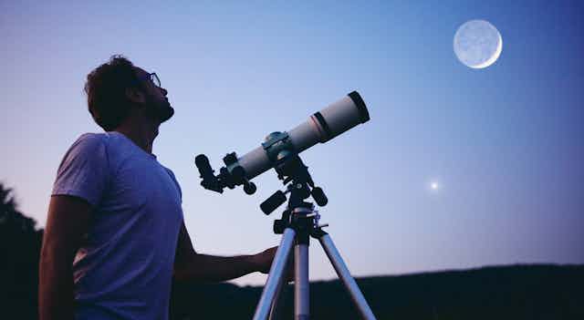 Man with telescope looks up to the sky.
