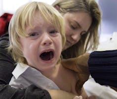 A blonde boy cries as he gets vaccinated.