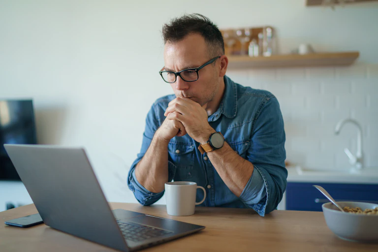 A man looks at his laptop while having breakfast.