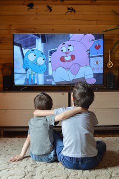 Two children sitting on the floor watching a cartoon.