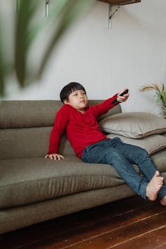 A child on a sofa pointing a remote control.