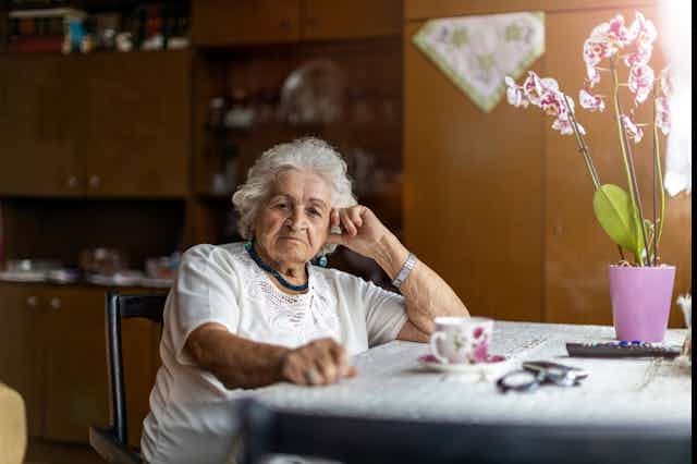 An elderly woman sits at the table at home.