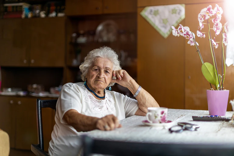 An elderly woman sits at the table at home.