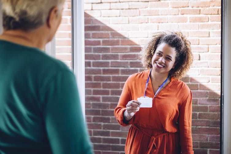 A smiling home-care worker is greeted by an older person at the front door.