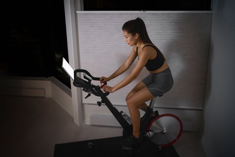 Woman riding a stationary bike while looking at a tablet.