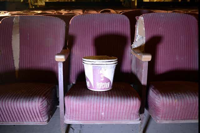 A stack of empty popcorn buckets on a purple chair in an abandoned cinema