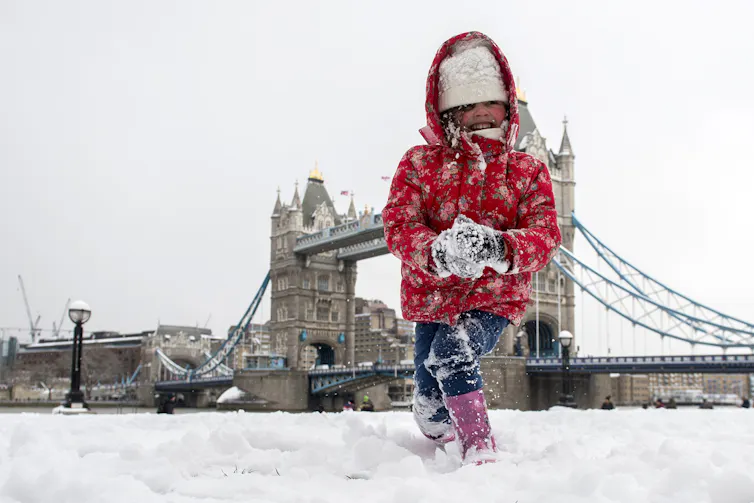 A young girl makes a snowball with London's Tower Bridge in the background.