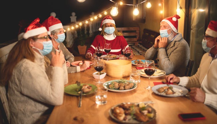 A family eating Christmas dinner wearing masks.