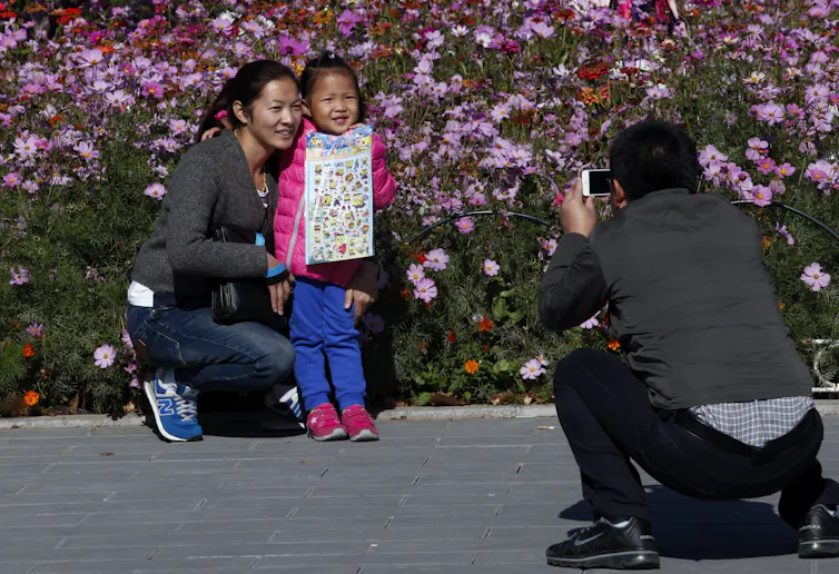 Man takes picture of woman and girl in front of pink flowers.