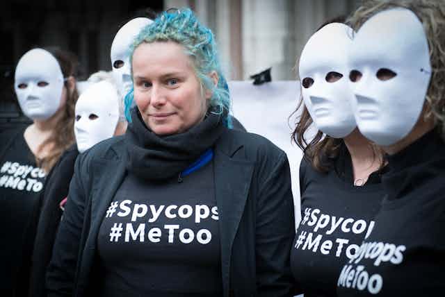 Kate Wilson, a victim of undercover police, standing in a group of other women wearing masjs and wearing wearing 'spy cops' t-shirts