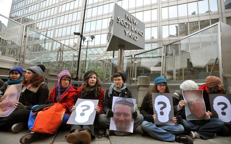 Protestors holding up photos of the undercover policemen who tricked them into having relationships.