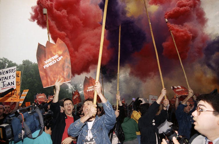 protesters holding signs with flare smoke in background