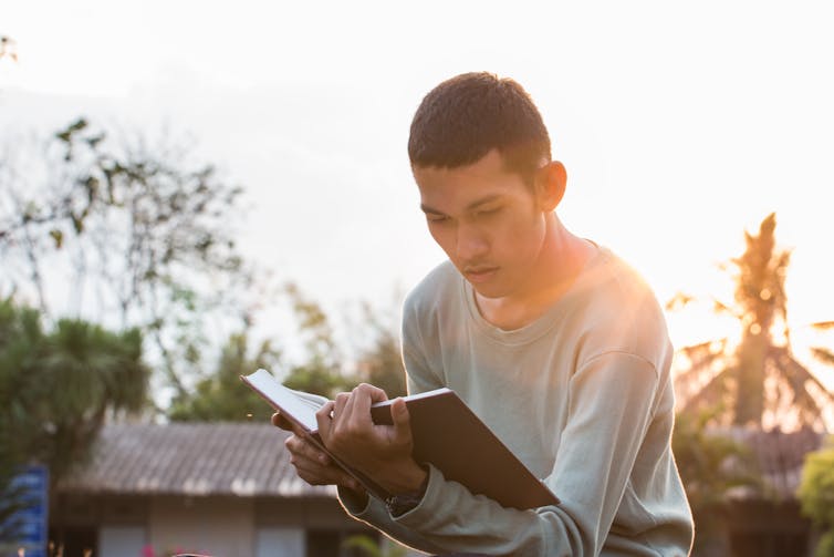 teenage boy reading book outside