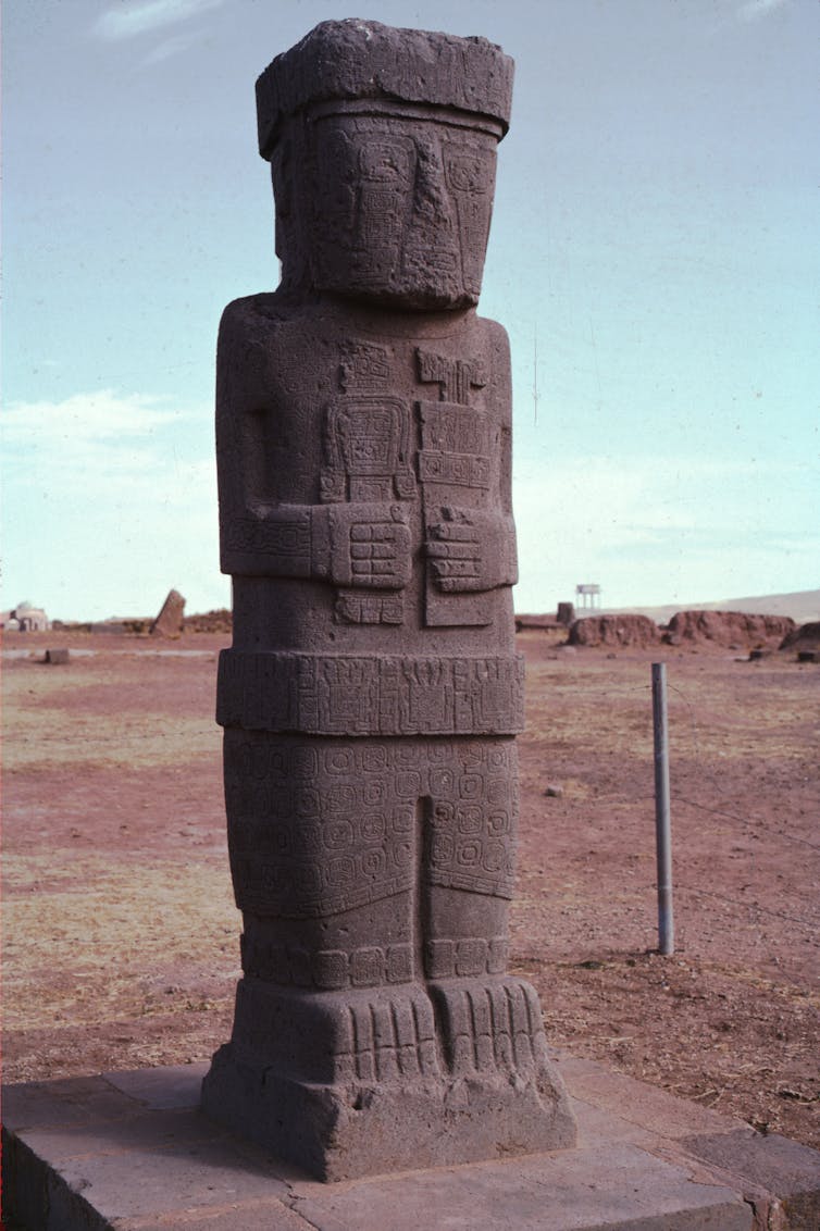 An intricately carved monolith of a person holding an item in each hand.