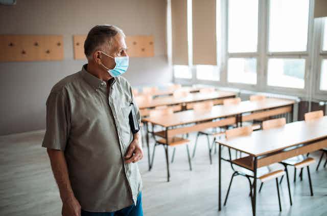 Profesor veterano con mascarilla en un aula vacía.