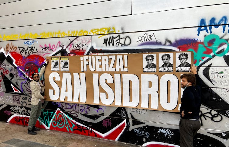 Two men hold la banner reaading 'Fuerza! San Isidro'