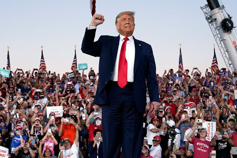 Trump stands in front of a crowd with his fist raised.