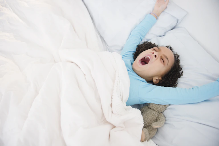 A young girl stretched her arm while lying in bed.