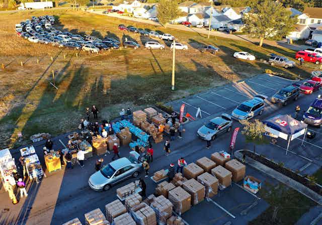 Aerial view of a parking lot with lots of cars and cardboard boxes and people standing around