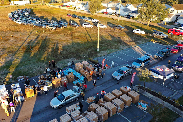 Aerial view of a parking lot with lots of cars and cardboard boxes and people standing around