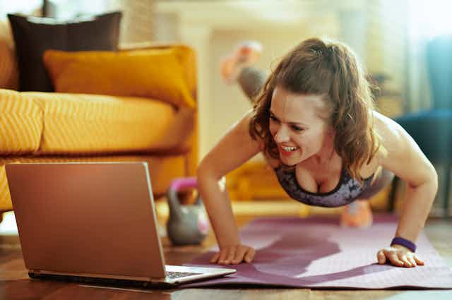 Una mujer hace flexiones en el suelo mientras mira un ordenador.