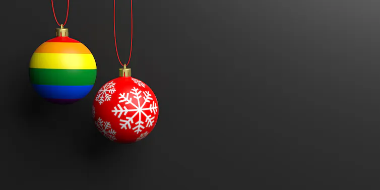One Christmas bauble with an LGBTQ+ flag next to a red bauble with a snowflake on it